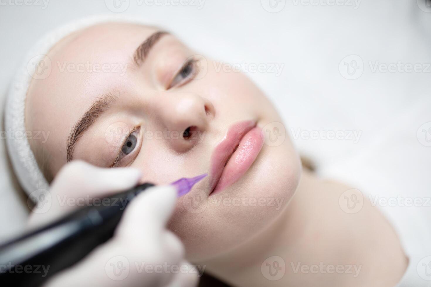 In a serene beauty salon, a woman receives a long-lasting makeup procedure. The technician carefully applies color to enhance her lips during this pampering session. photo