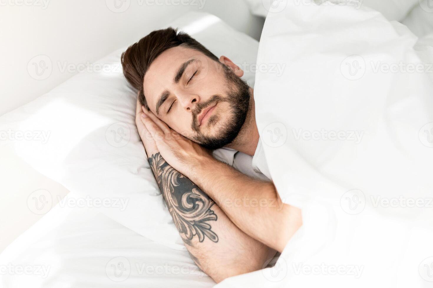 Deep male sleep. Asleep young guy sleeping resting peacefully in his comfortable bed at home. Man lying with eyes closed. Recreation, time to rest and nap concept photo