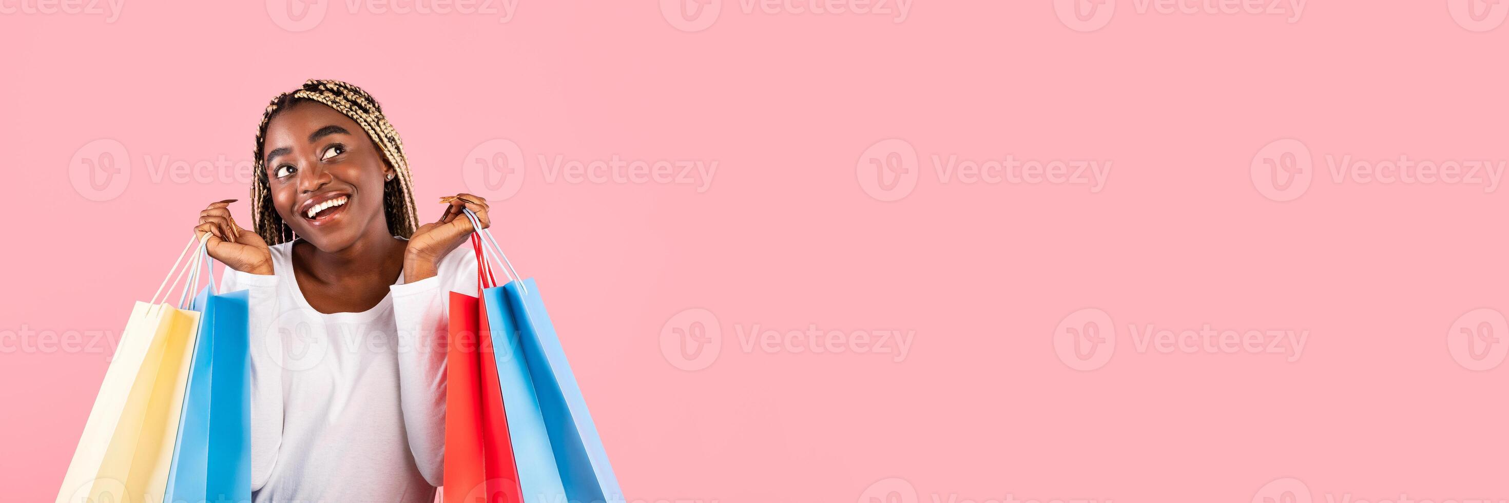A young woman joyfully holds colorful shopping bags while smiling. She showcases her excitement for Black Friday deals, surrounded by a vibrant pink background with empty space for text. photo