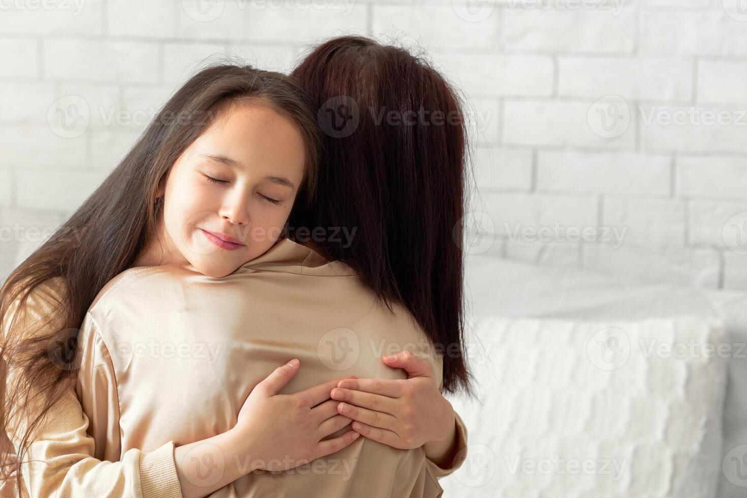 Affectionate teen girl in homewear embracing her mother on bed indoors. Cute kid expressing her love to mom, hugging her in bedroom. Building strong family relationships concept photo