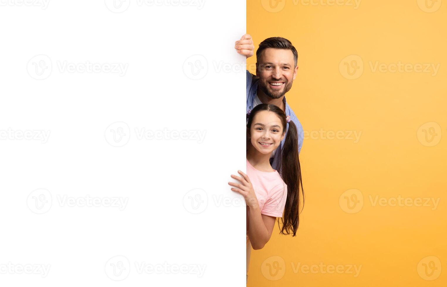 A father and daughter express love and happiness as they peek from behind a blank surface. Surrounded by a bright yellow background, their smiles radiate warmth and affection. photo