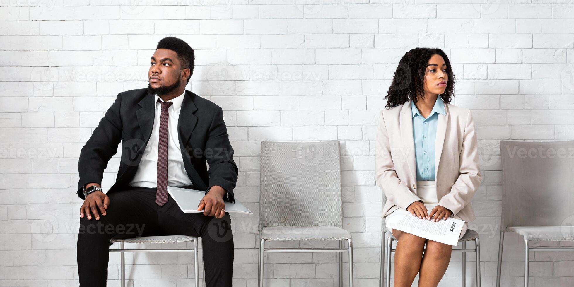 Black man and woman in formal wear looking in opposite directions, feeling competitive while waiting for job interview at office lobby. Vacancy fair, staff recruitment concept photo