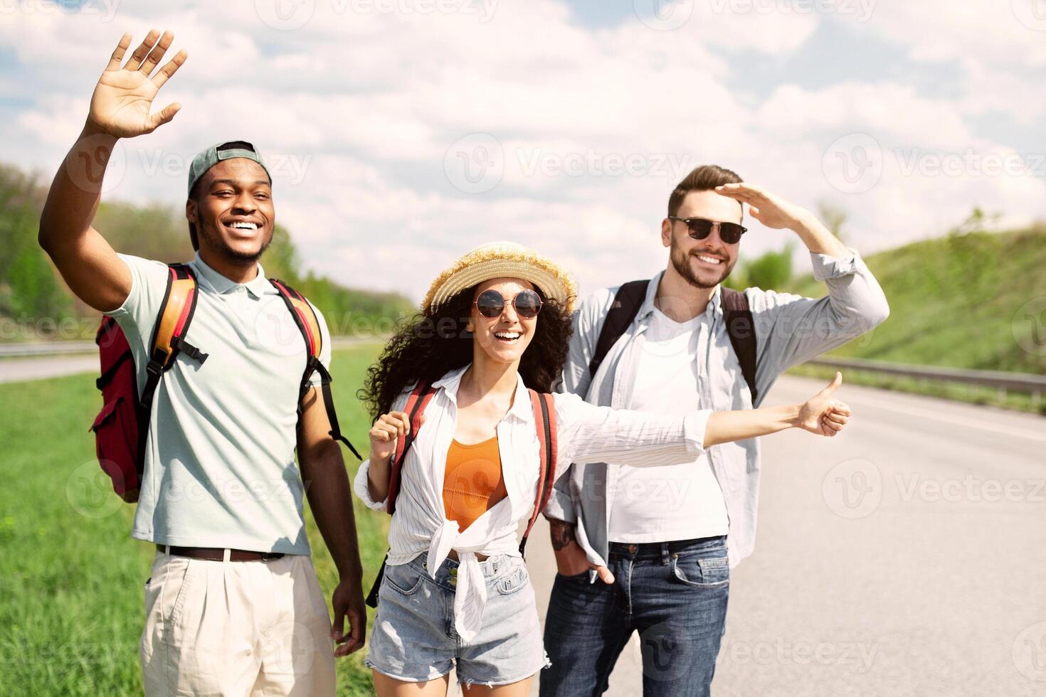 Exciting travel adventure, hitchhiking with friends, summer holidays concept. Millennial people standing on roadside, stopping car, trying to get free ride, having autostop journey, copy space photo