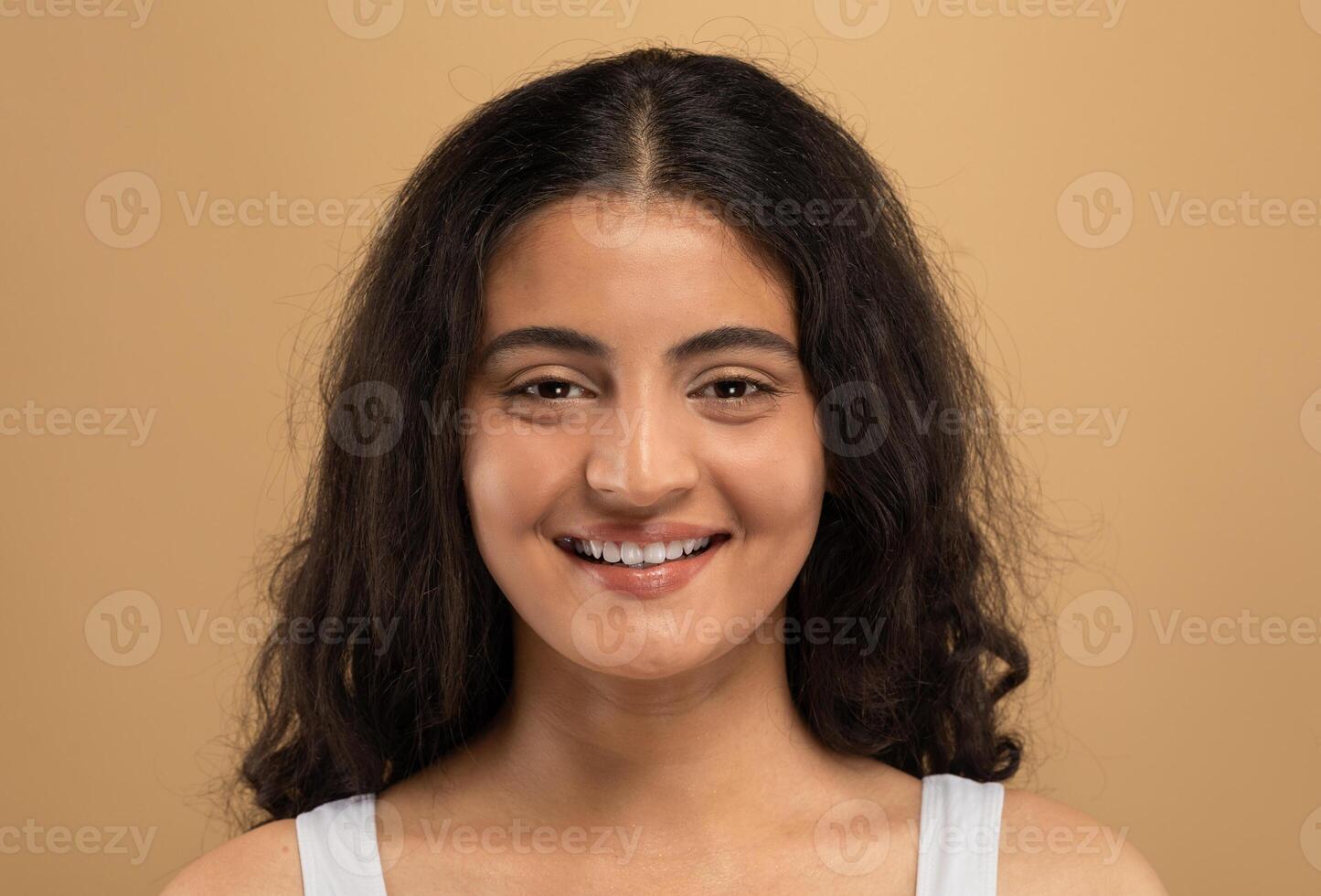 A young Eastern Indian woman enjoys a skincare session in a cozy, isolated setting. She is focused on her beauty routine, showing a radiant smile and glowing skin. photo