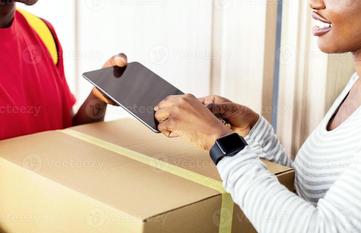 Parcel Delivery. Black Lady Receiving Delivered Parcel From Male Courier Putting Finger To Tablet Scanning Fingerprint For Identity Verification Standing At Home. Cropped, Selective Focus photo