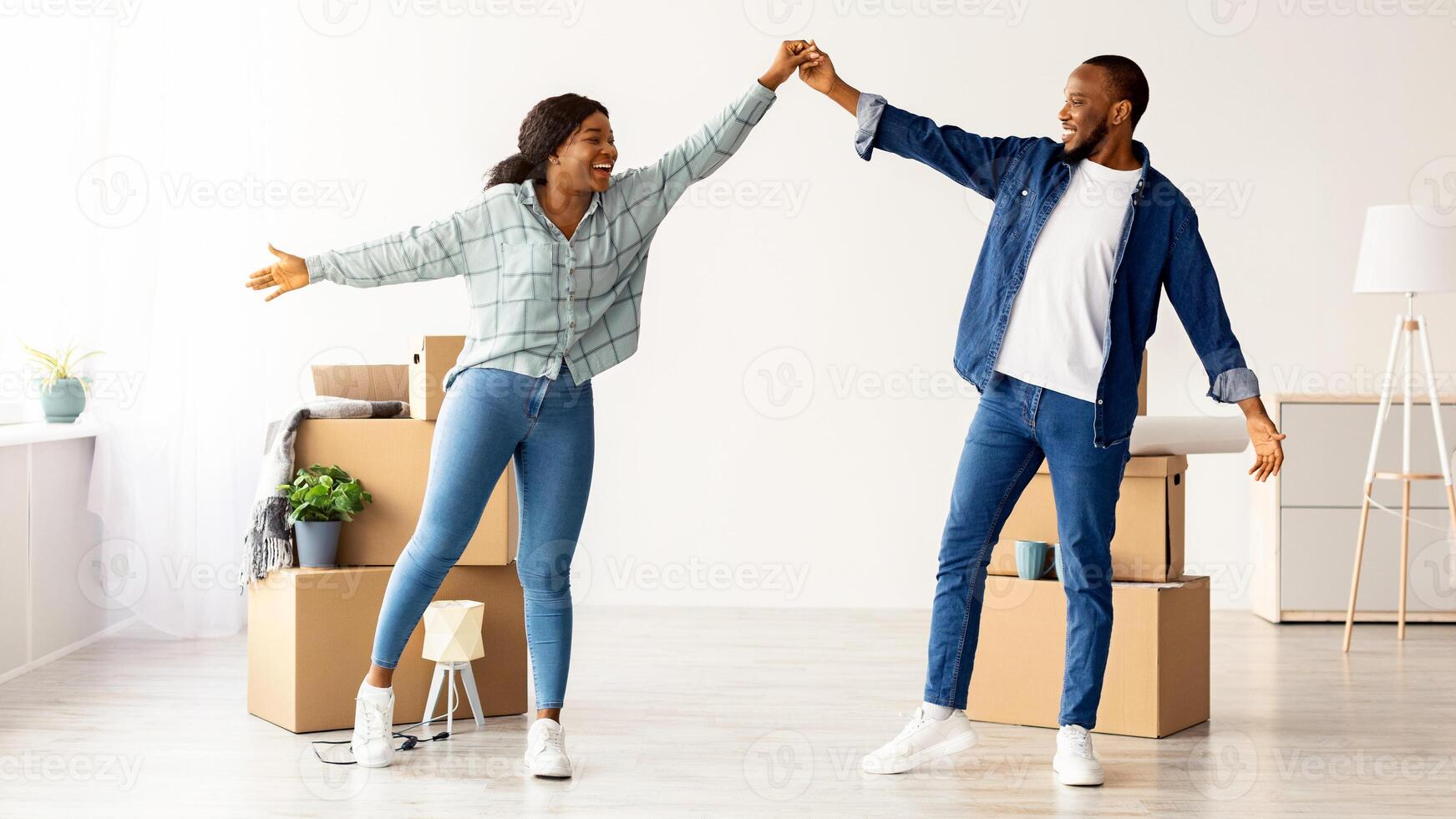Moving Day. Joyful African American Spouses Dancing Among Cardboard Boxes In Their New Apartment, Happy Young Black Spouses Celebrating Relocation To Own Flat, Full Length Shot, Free Space photo