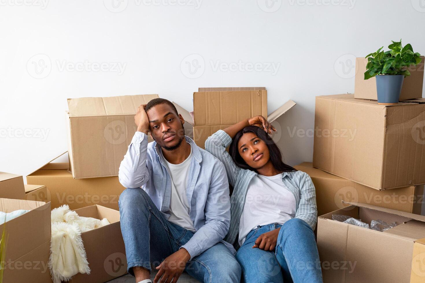 Sad black spouses exhausted after moving to new apartment, sitting among cardboard boxes and resting, having problems during relocation to own home photo