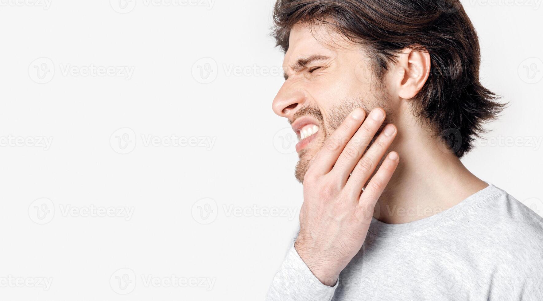 Not tolerate pain in teeth and dentures. Man suffers from pain and presses his hand to cheek, panorama, cropped, studio shot photo