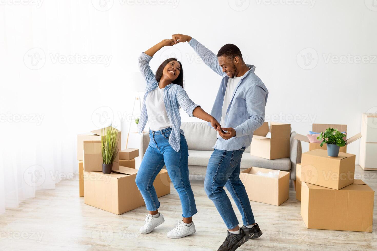 Happy affectionate black spouses dancing in their new apartment among cardboard boxes on moving day, free space. Positive sweethearts having fun while relocating to new house photo