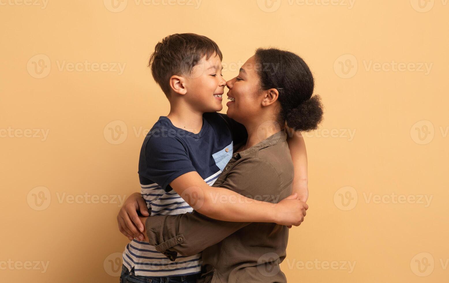 A mother and her son embrace each other happily against a warm, neutral background. Their smiles reflect love and affection, showcasing the special connection they share as family. photo