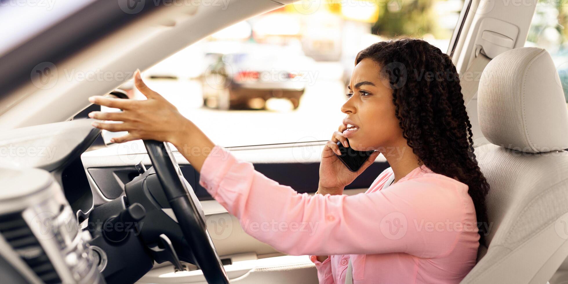 Portait of angry African American woman talking on mobile phone while driving car, stressed irritated female driver using her cellphone, unhappy lady arguing and riding in the city, profile side view photo