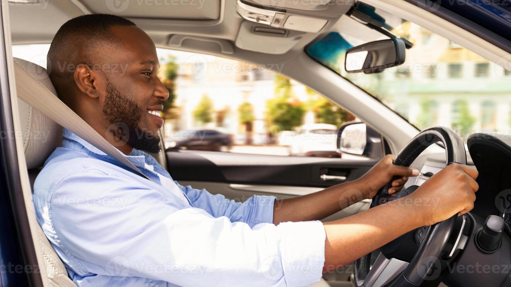 Side view profile portrait of joyful African American man driving car, going to work or on trip during summer vacation. Happy guy riding his brand new nice car, doing test drive in dealership showroom photo