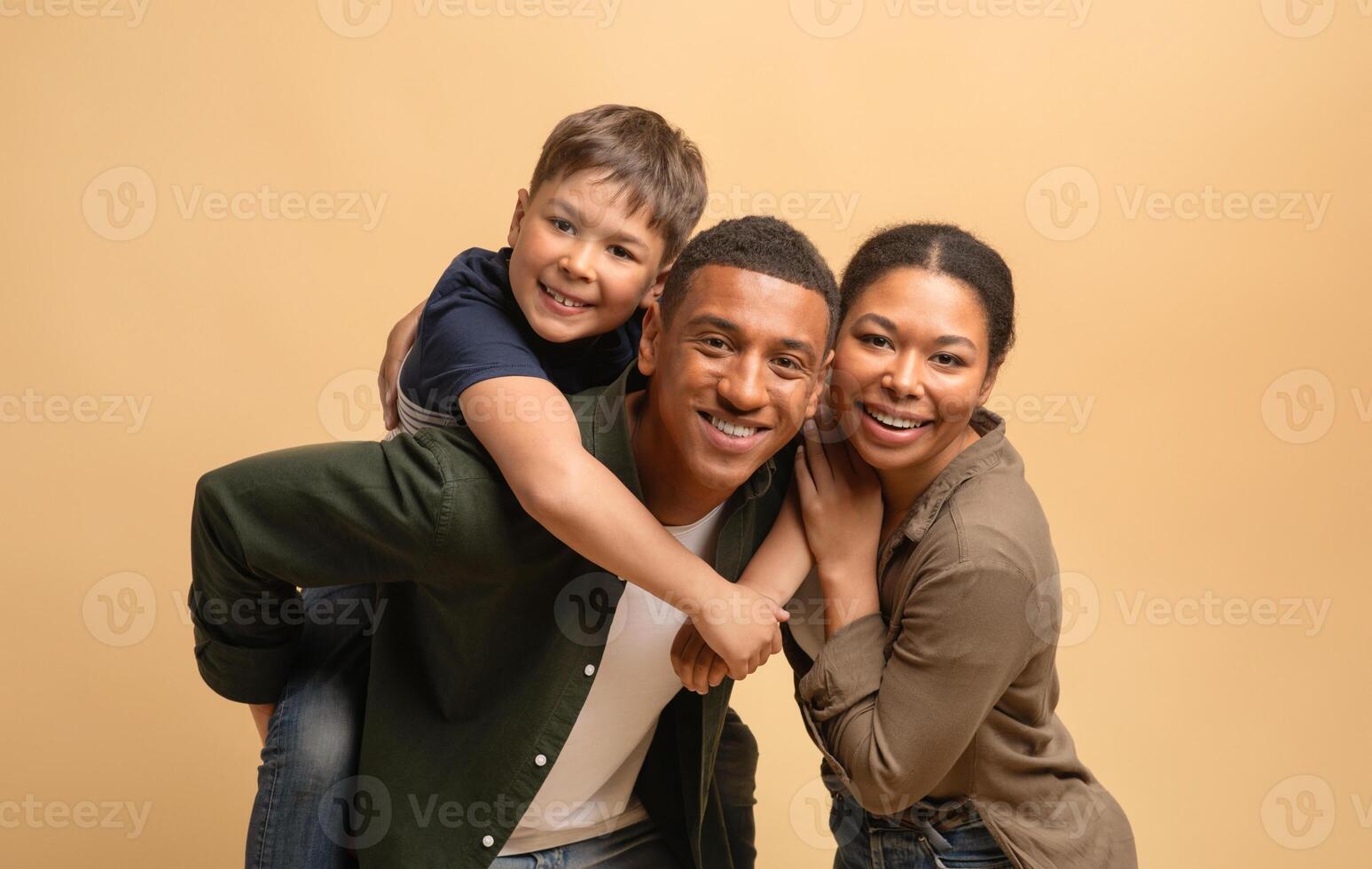 A father, mother, and their teenage son share a moment of happiness and connection. The family poses closely, smiling warmly at the camera, radiating love and unity against a soft backdrop. photo