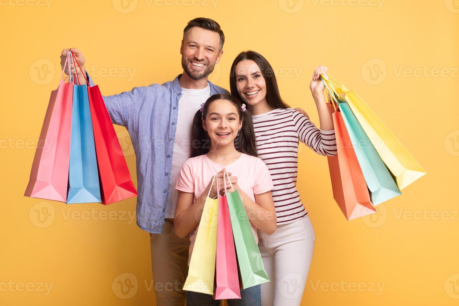 A cheerful family consisting of a mother, father, and teenage daughter poses happily, holding colorful shopping bags. They display love and connection in a vibrant setting. photo