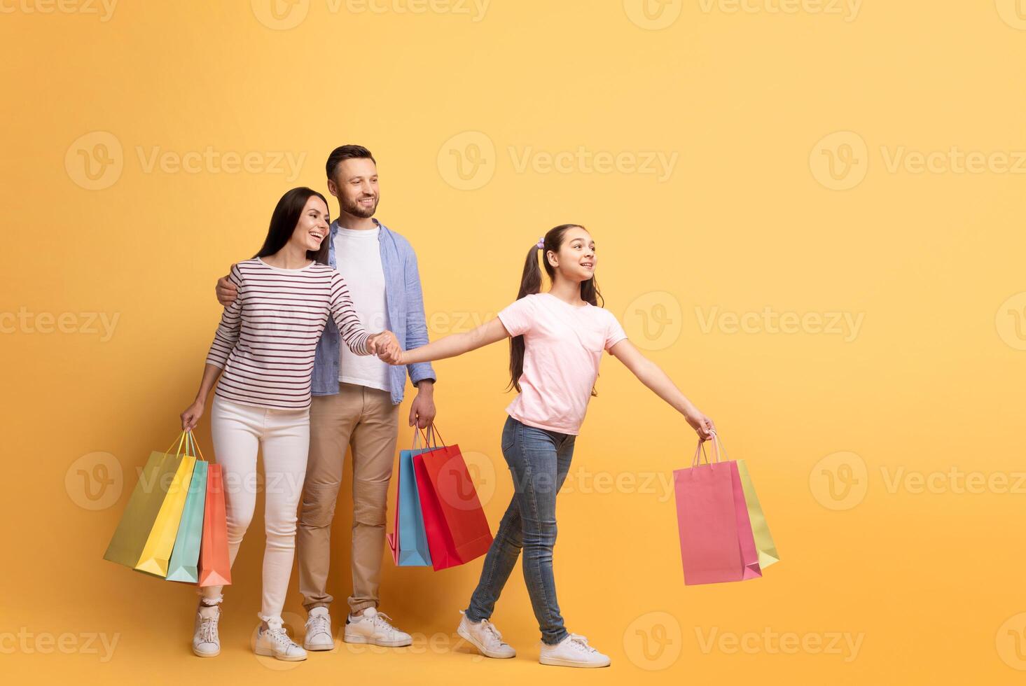 A happy family of three, including a mother, father, and teenage daughter, share smiles while shopping. The daughter leads with colorful bags, showcasing family bonding and affection, copy space photo