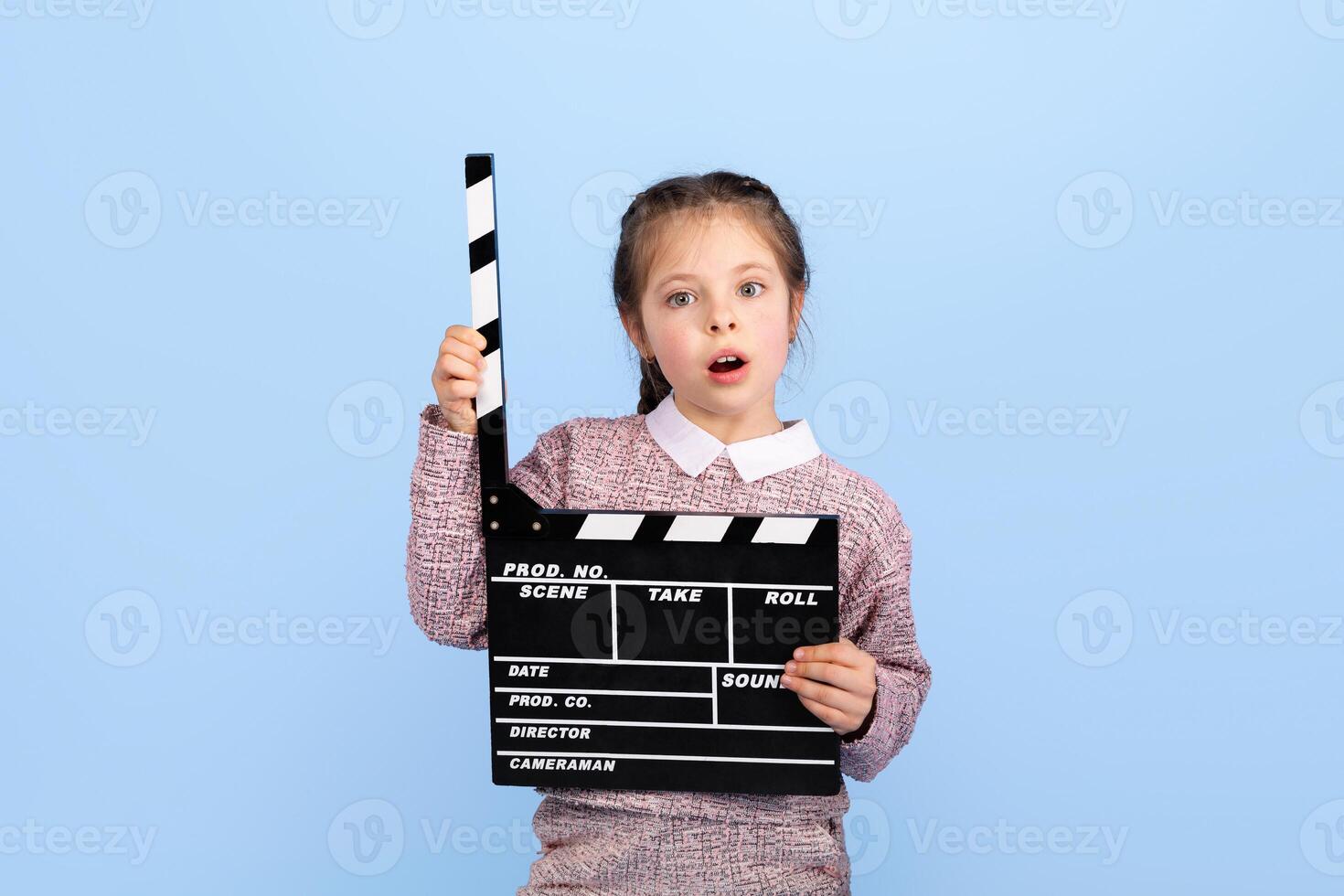 A joyful girl expresses excitement while holding a clapperboard, indicating her role in a creative project. The setting is bright and isolated, enhancing her joyful demeanor. photo