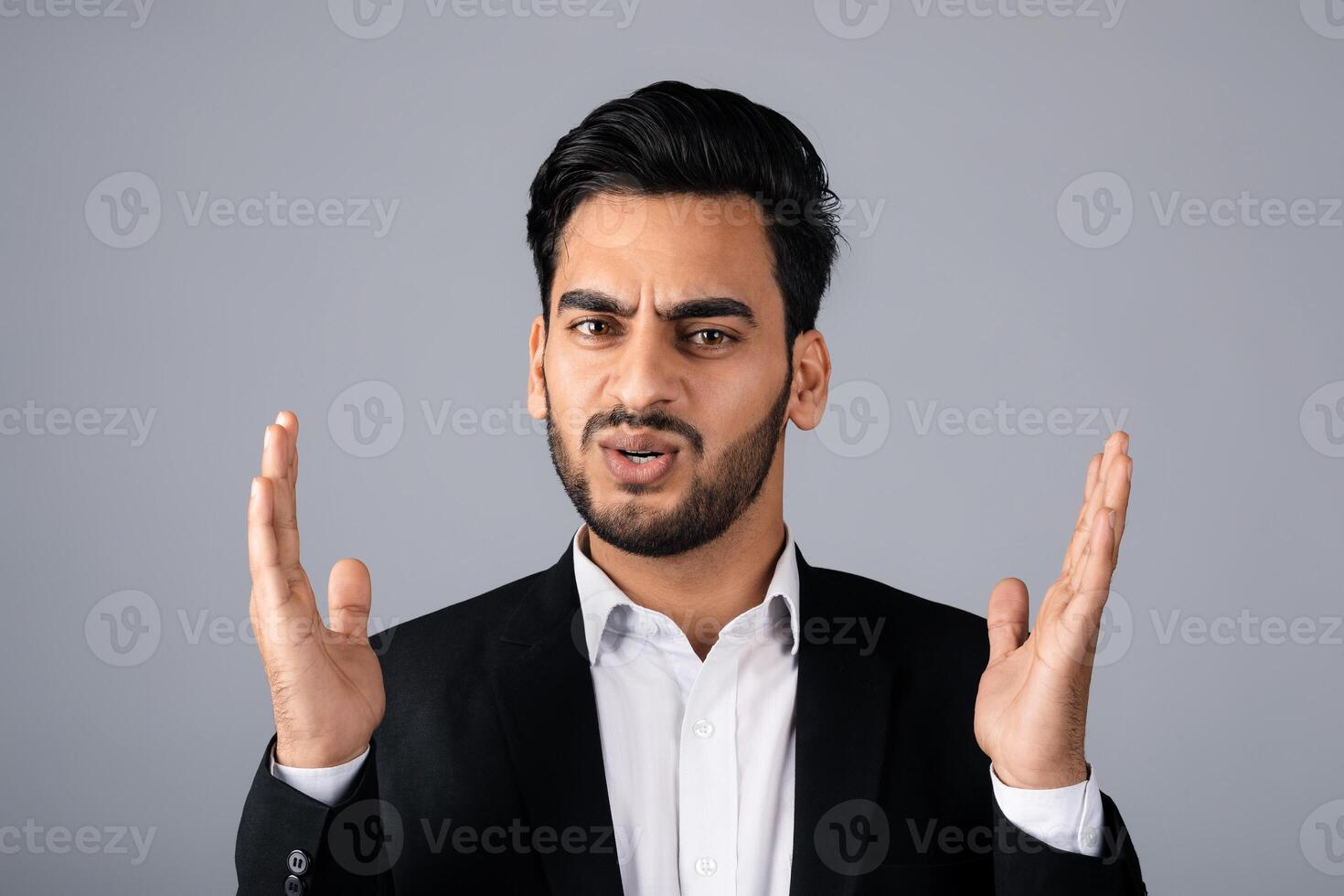 A Middle Eastern businessman in a suit conveys surprise with his hands raised. He is in a studio setting, focusing on entrepreneurial concepts and corporate strategies. photo