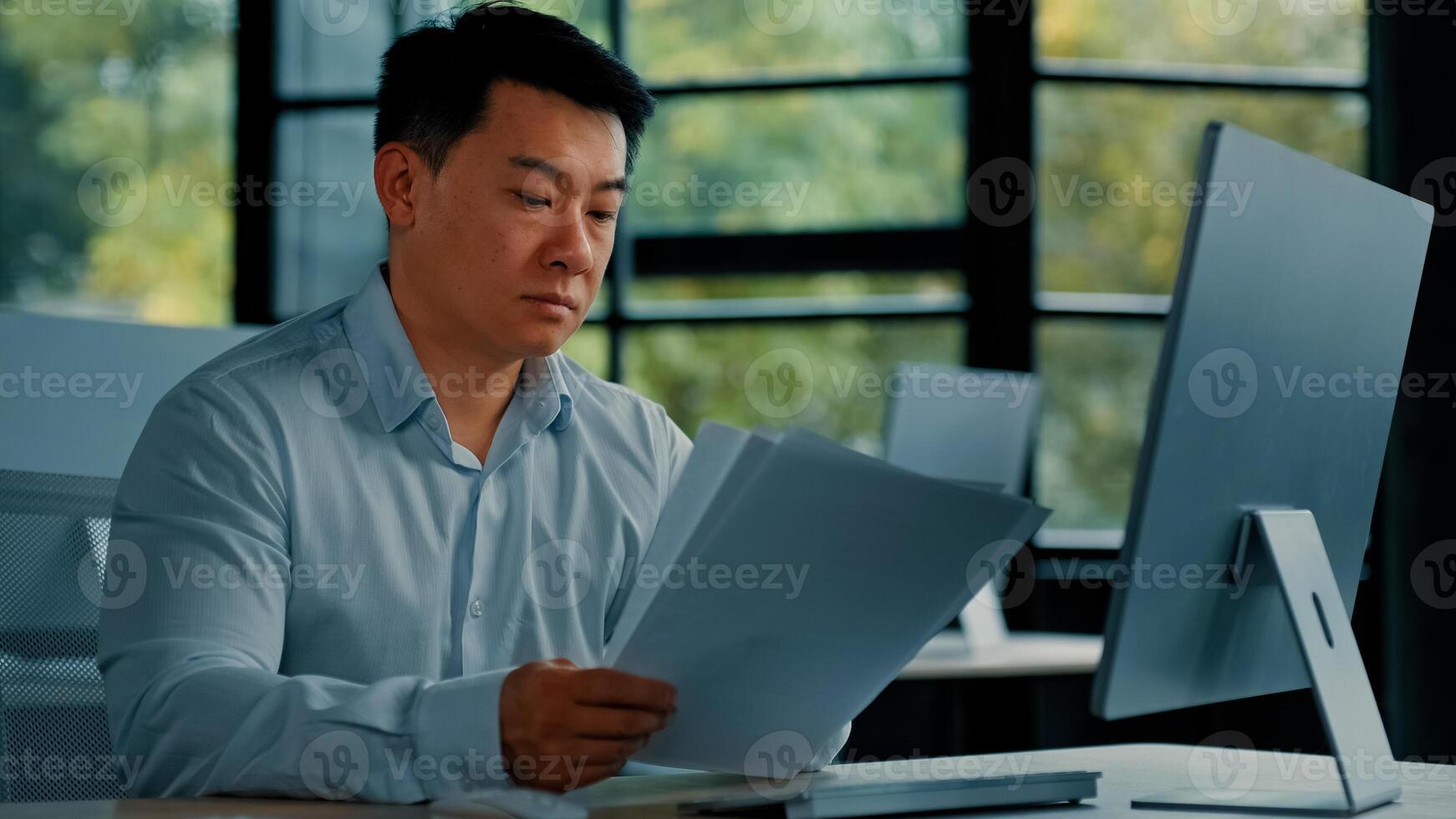 Professional asian businessman korean japanese 40s man lawyer office worker reading financial documents invoice contract budget documentation searching business data at computer paying bills online photo