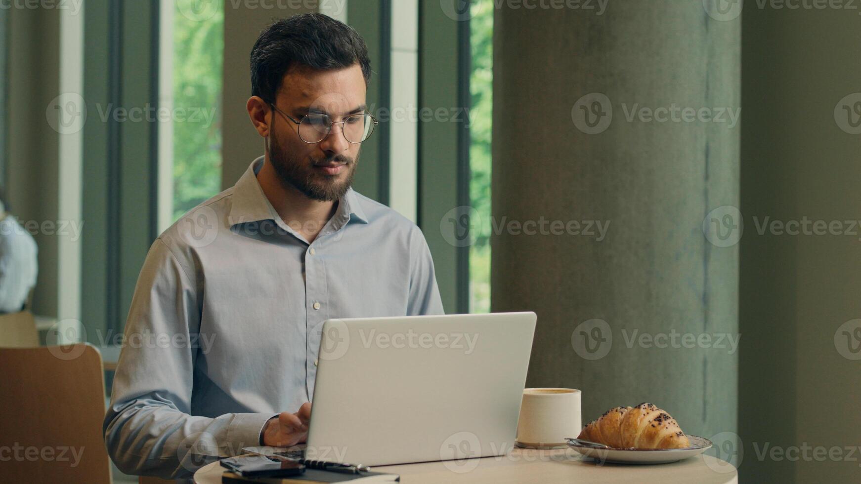 Arabian Indian man typing laptop keyboard concentrated business guy male businessman at cafe table online work computer browsing internet write tasks thinking freelancer manager employee distant study photo
