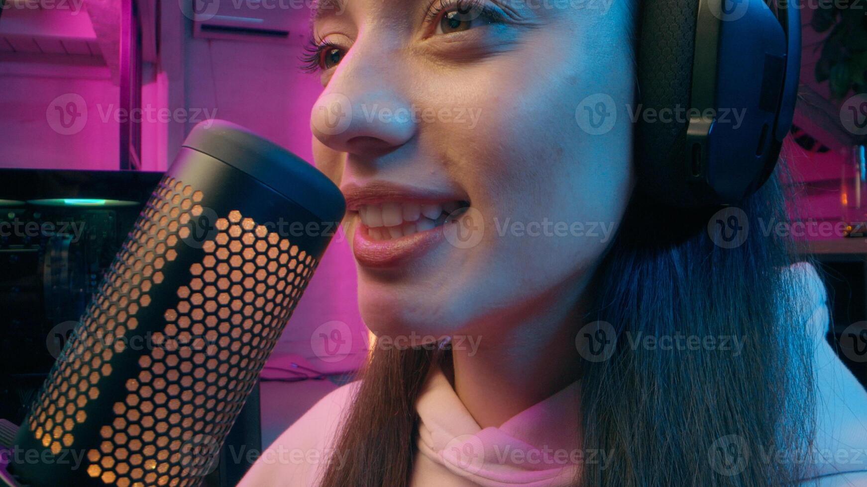 Joyful Caucasian girl host woman influencer blogger female vlogger hold microphone stream at home neon addict streamer presenter talk radio broadcast play online game computer cyber sport blog photo