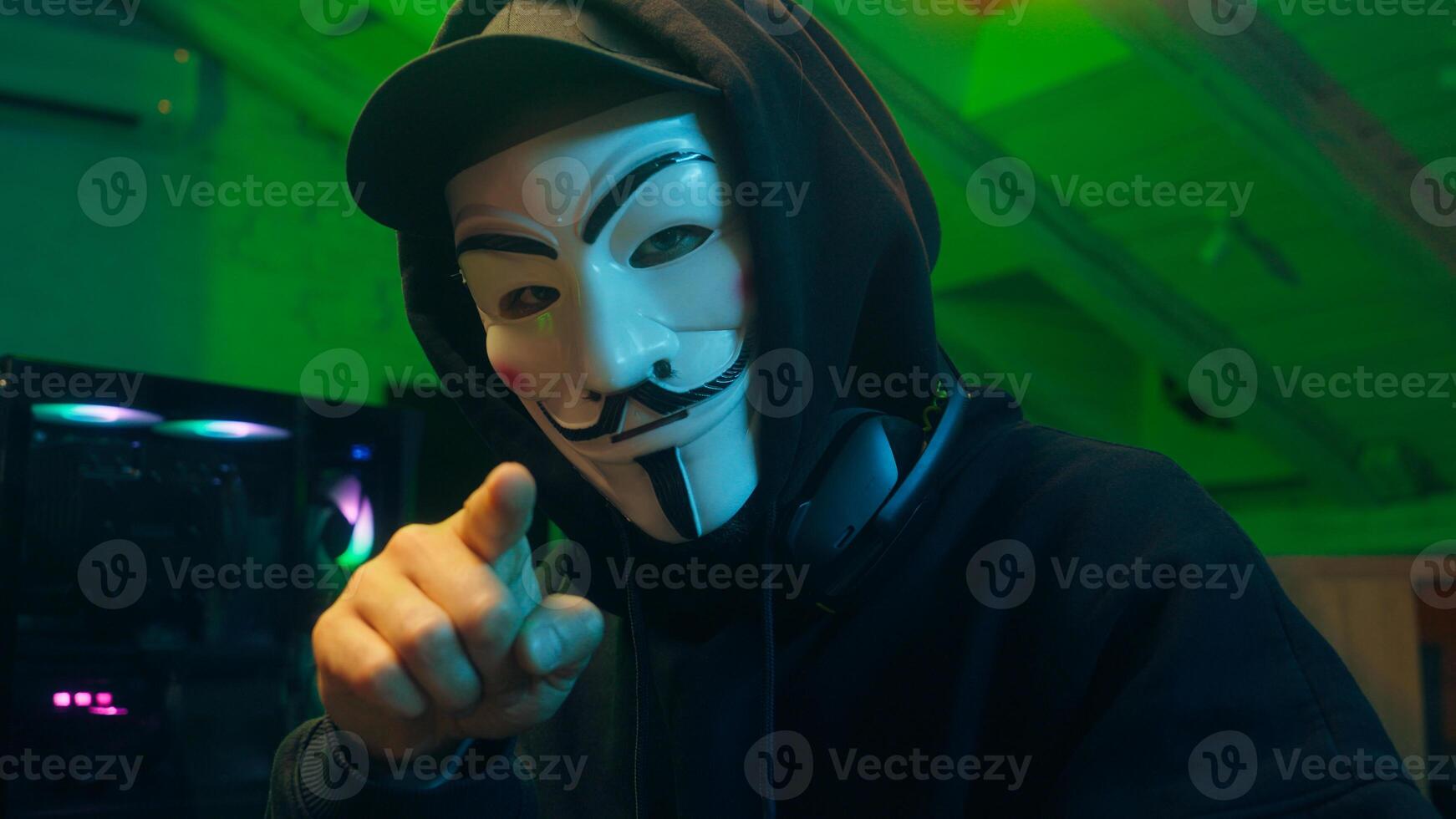 Lviv, Ukraine - June 03, 2024. Hacker anonymous typing computer looking at camera pointing finger programmer attack cyberspace fraud burglar internet spyware virus pc scam network binary code firewall photo