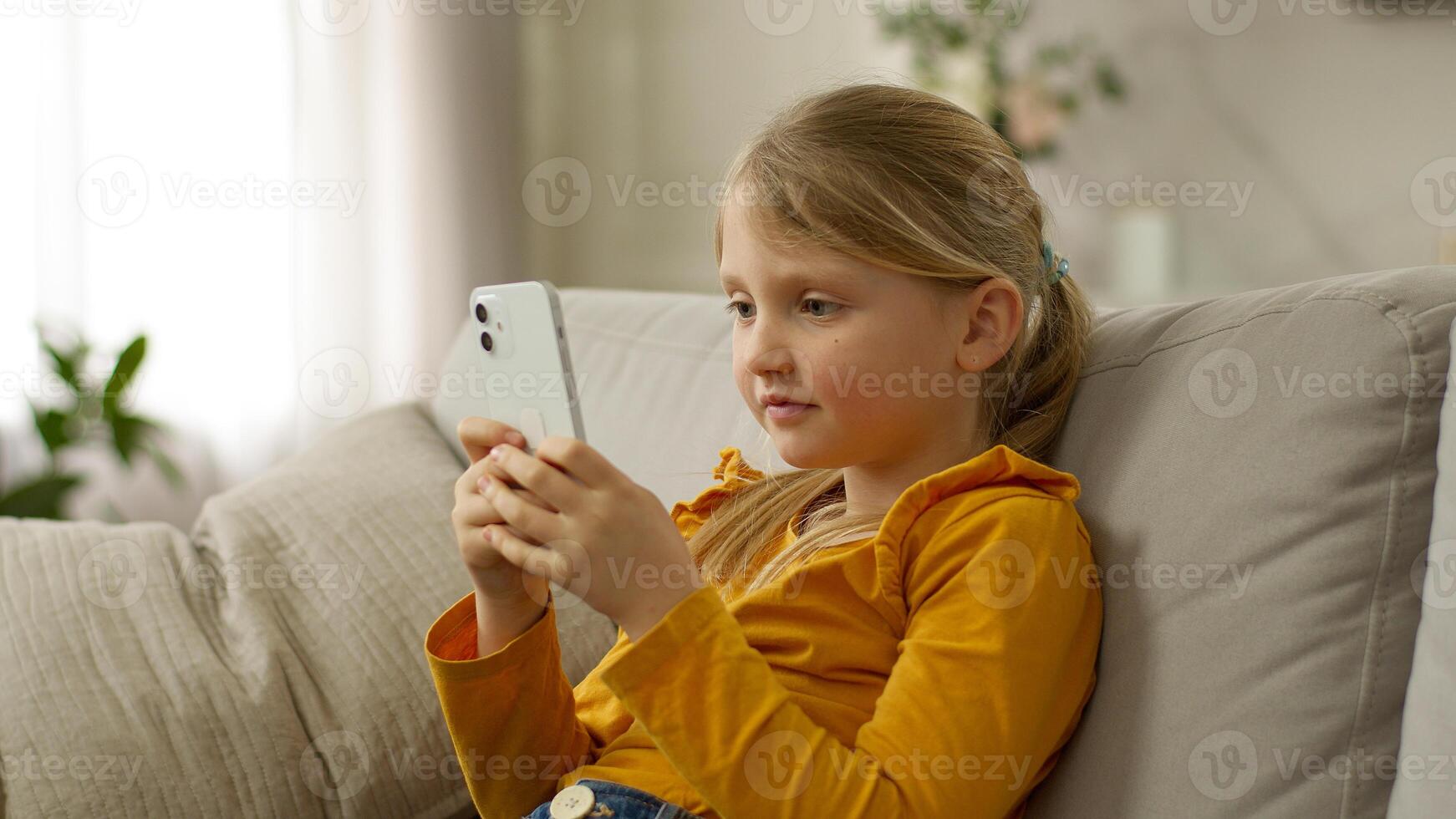 Happy little girl sofa holding mobile phone smartphone rejoice good news winning victory excited enjoy child kid successful celebrate joyful technology yes luck gadget home delighted female cellphone photo