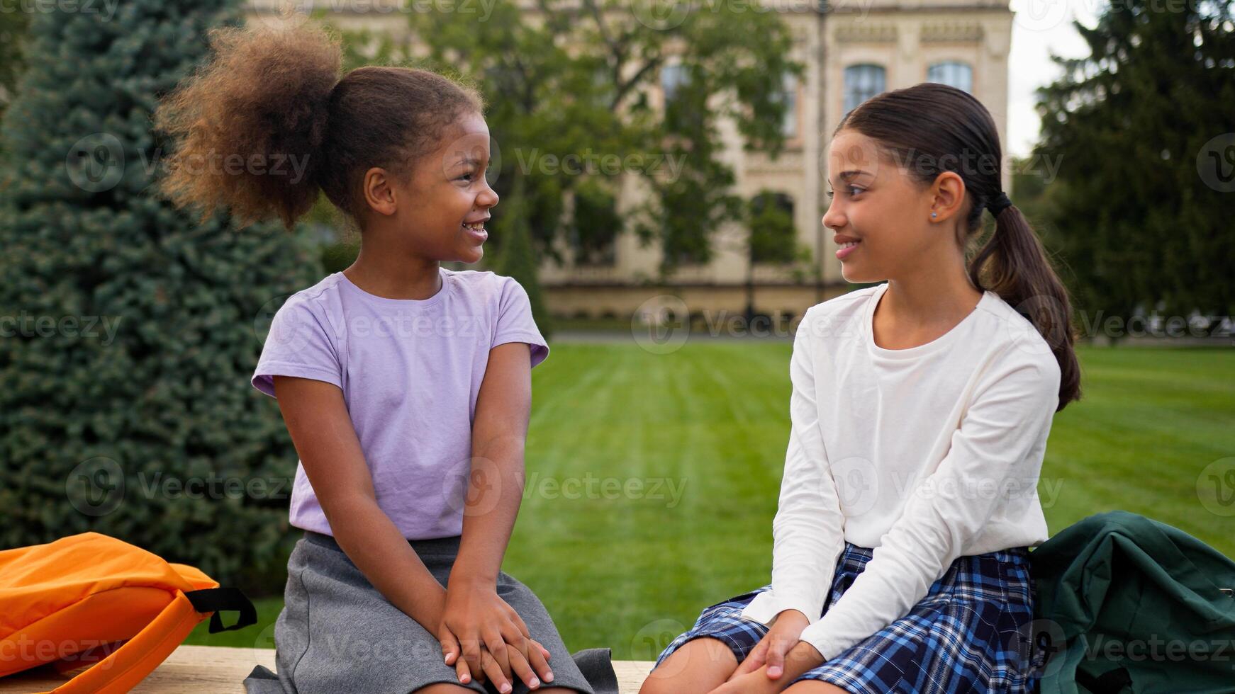 Smiling schoolgirls classmates female friends little girls children kids school education outdoors talk chat friendly conversation multiethnic happy African Indian teen sisters students study outside photo