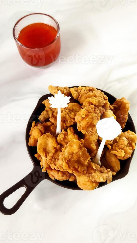 A delicious bowl of crispy fried chicken tenders served with a side of tangy dipping sauce. photo