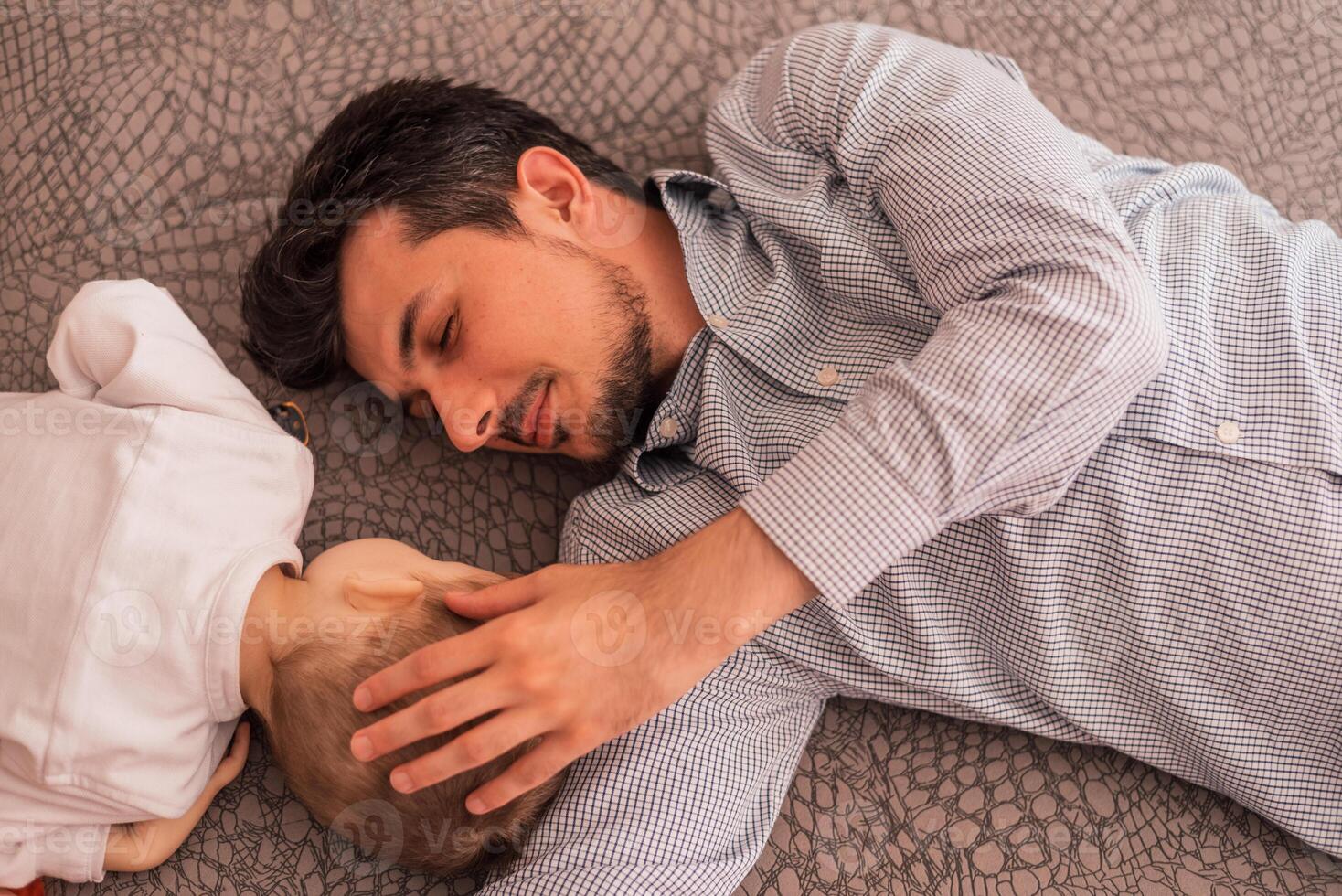 A young father shares love with his son and spends time together at home, lying on the bed, top view. photo