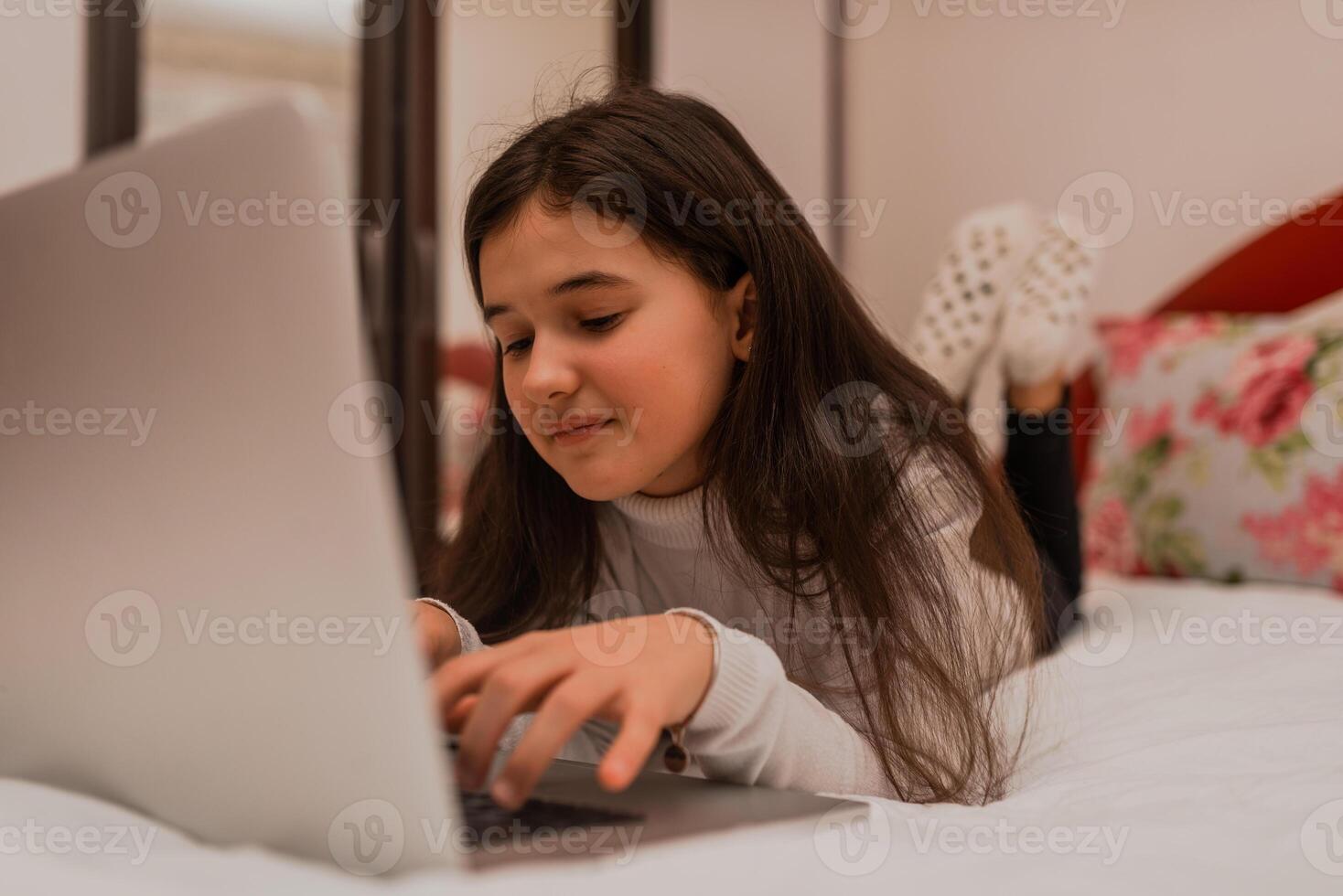A happy teenage girl using a laptop while comfortable lying on the bed at home. photo