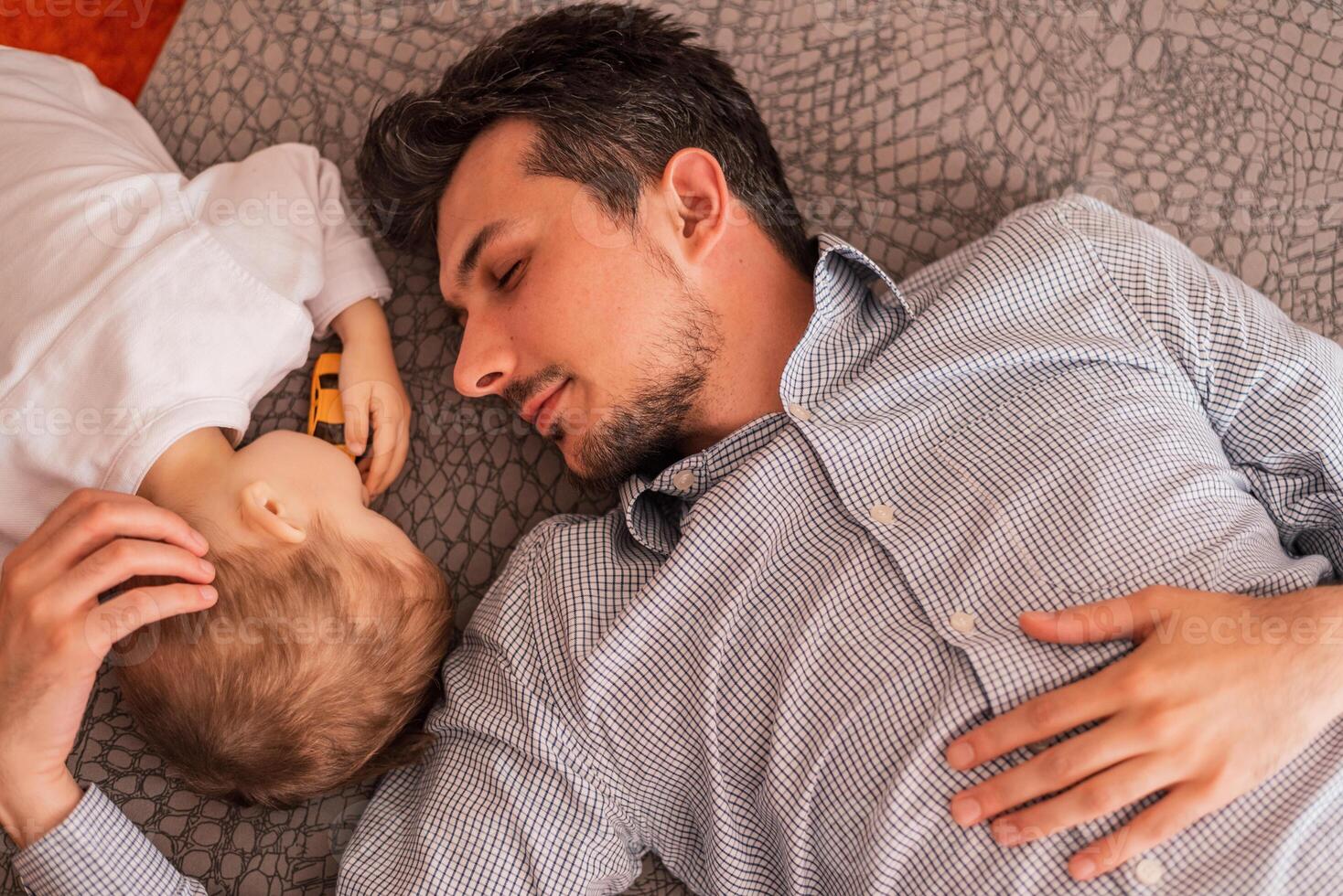A young father shares love with his son and spends time together at home, lying and sleeping on the bed, top view. photo