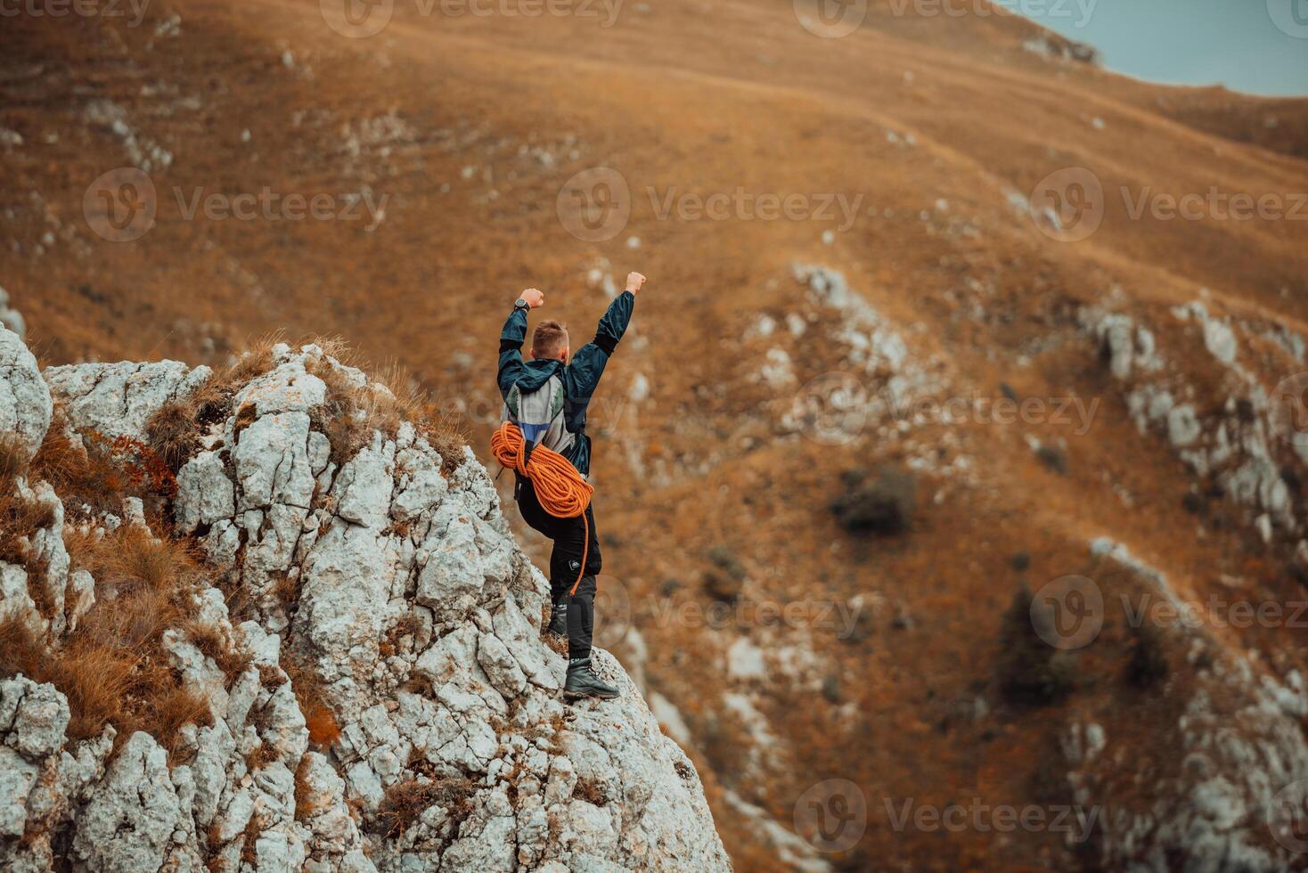 A male climber with arms up celebrating successful completed route on the top mountain peak cliff, adventure travel. photo