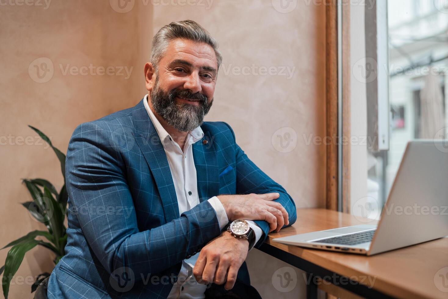 A happy mature businessman working on a laptop in the office or cafe restaurant, looking at a camera and smiling. photo