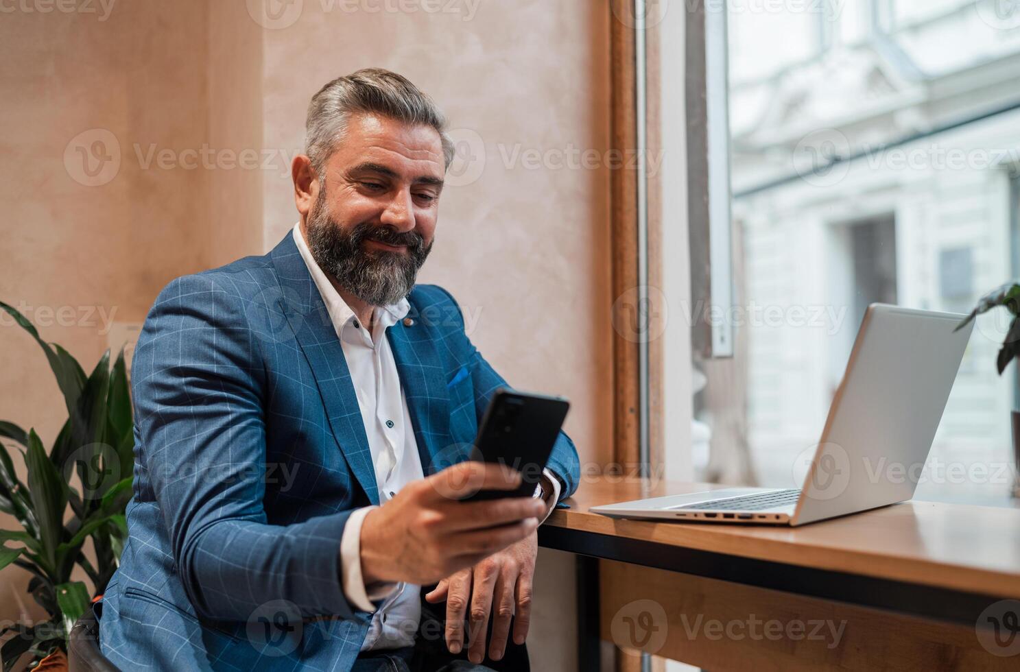 A happy mature business man using his phone while working on a laptop in the office or cafe restaurant. photo