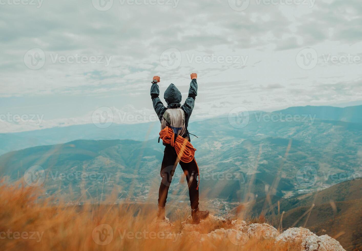 A male climber with arms up celebrating successful completed route on the mountain top, adventure travel. photo