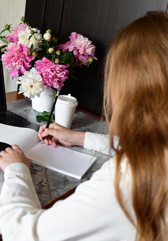 A woman with long brown hair is sitting at a table and writing in a notebook. photo