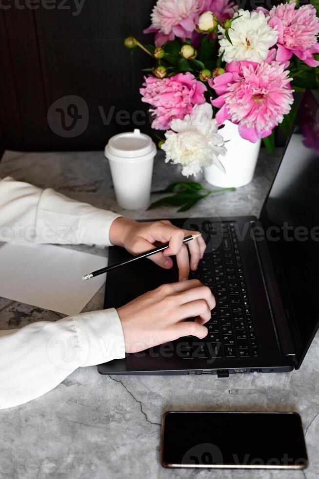 A woman is working on a laptop in a cafe. There is a coffee cup and a phone on the table. photo
