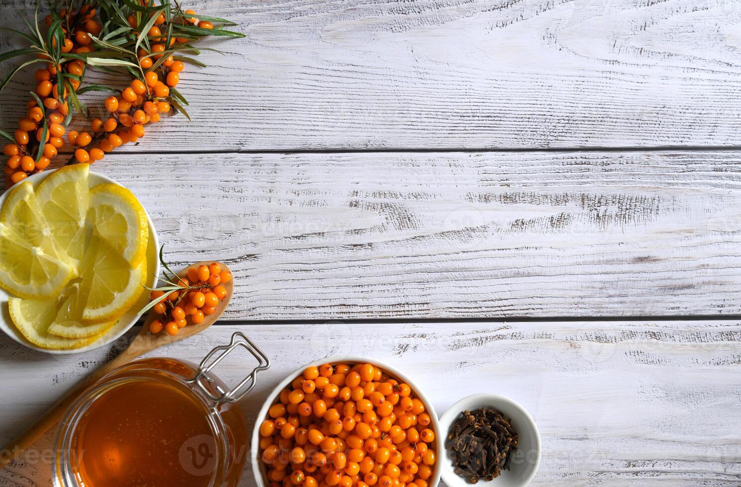 A flat lay of ingredients for a healthy and flavorful drink, including sea buckthorn berries, lemon slices, honey, and cloves, all displayed on a rustic wooden background. photo