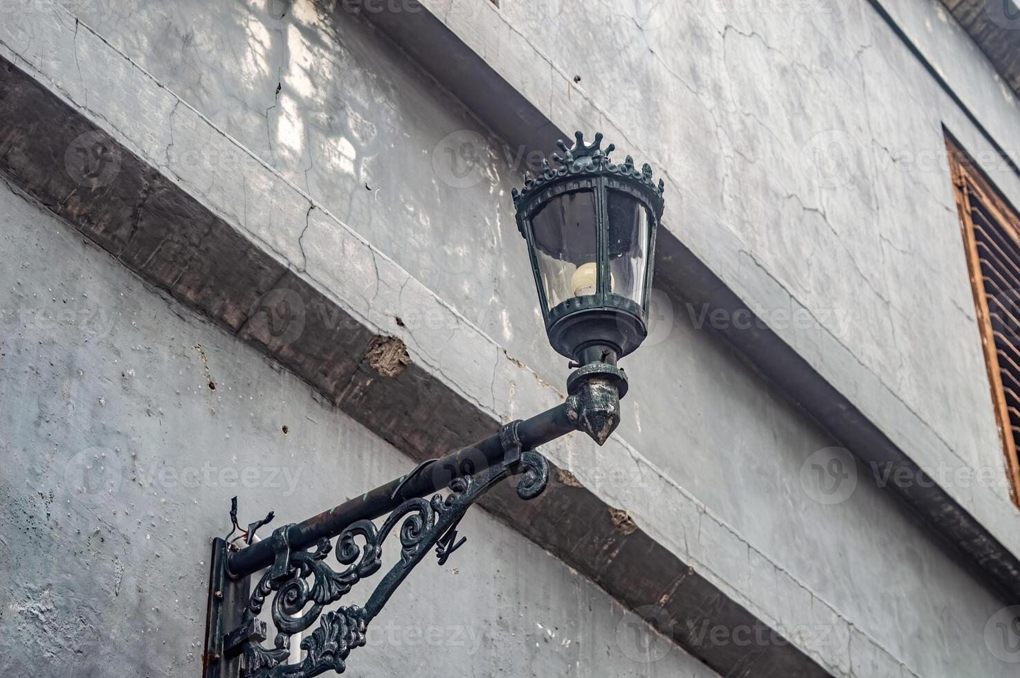 A vintage street lamp mounted on a weathered wall with intricate metalwork, showcasing urban decay and historical charm photo