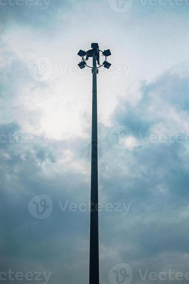 A tall street light pole with multiple floodlights against a cloudy sky, creating a dramatic and moody atmosphere photo