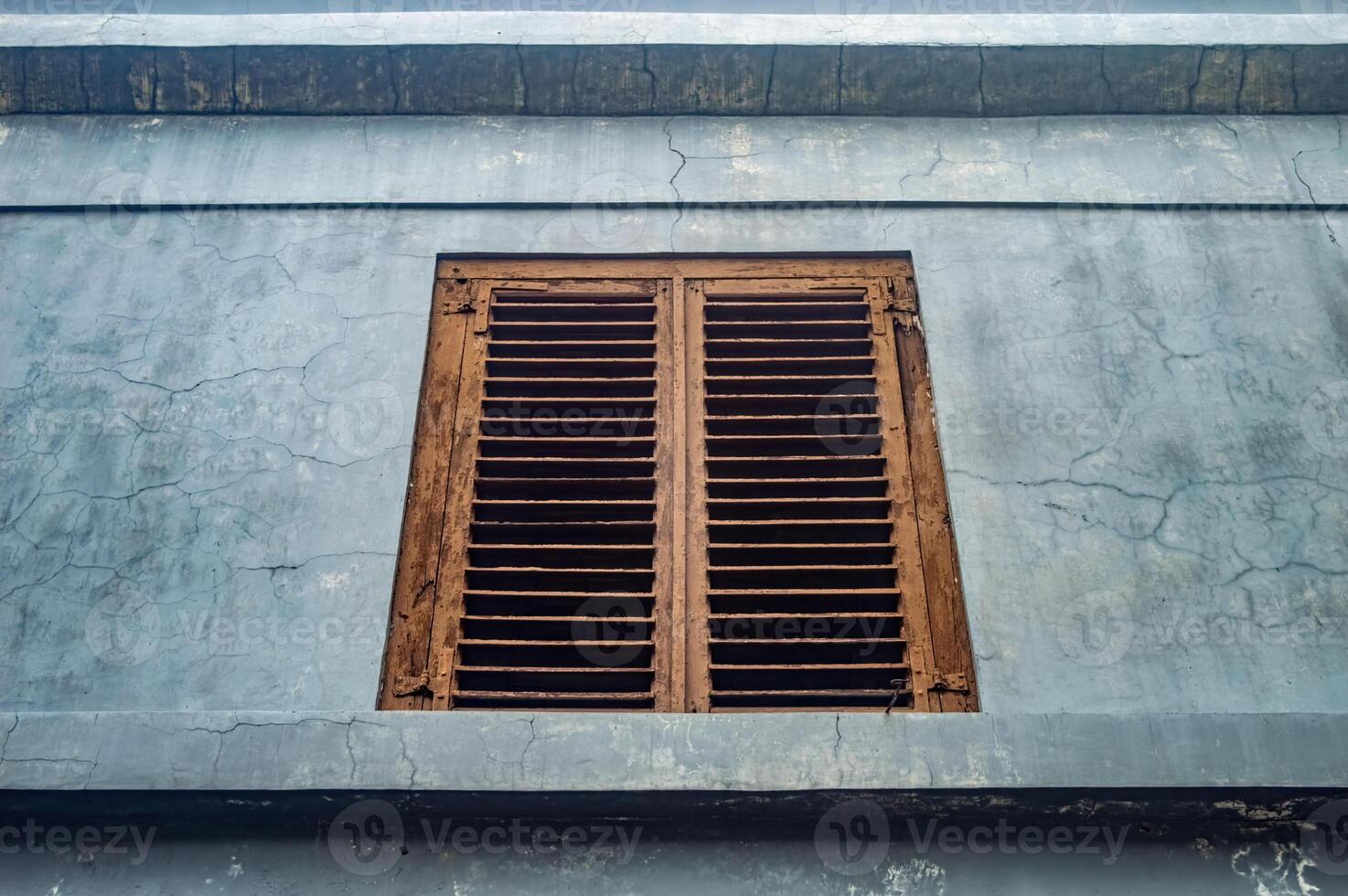 An old, weathered wooden window shutter on a cracked, faded blue wall. The rustic charm and aged texture make it a captivating subject for vintage and architectural photography photo