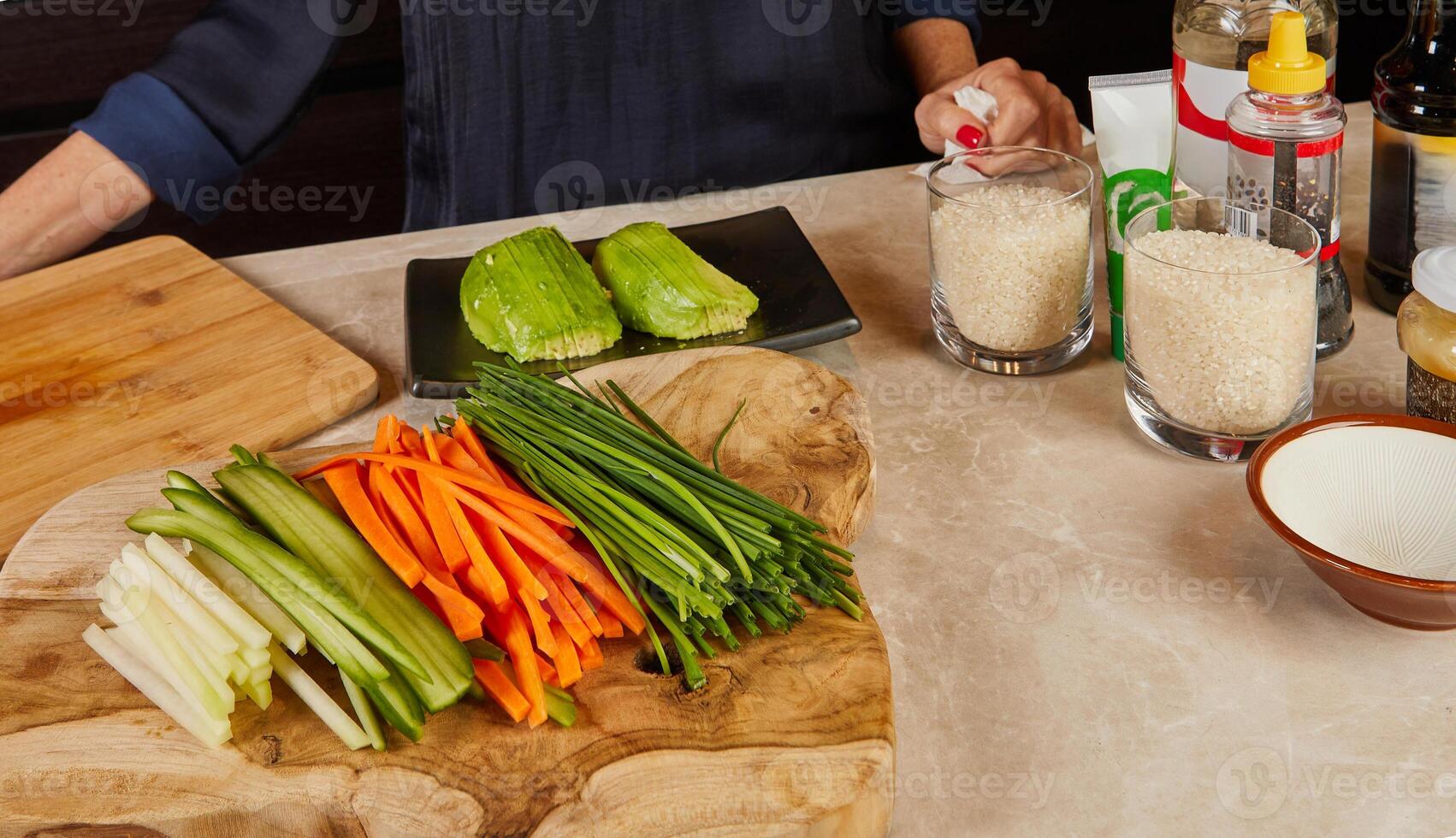 A beautifully arranged wooden board with sliced vegetables, avocado, and sushi rice in glasses, set for sushi making in a kitchen. photo