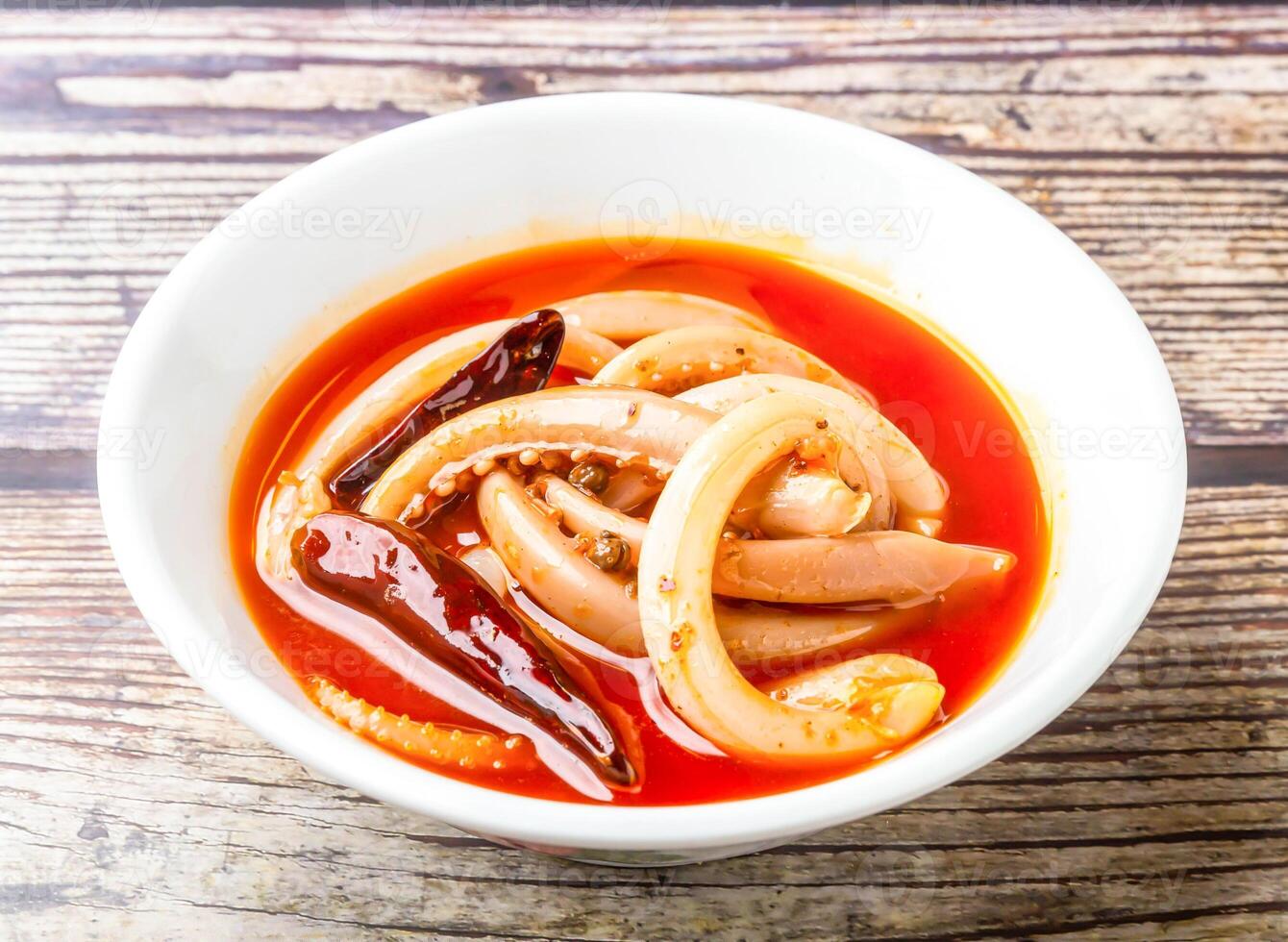 Spicy squid tentacles with red chilli served in bowl isolated on wooden table side view of hong kong food photo