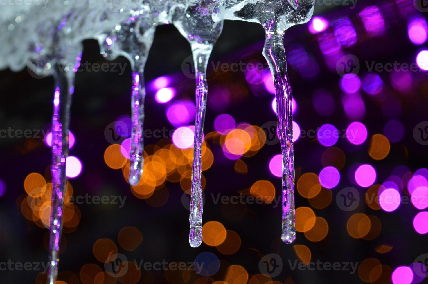 beautiful icicles on THE BACKGROUND OF CHRISTMAS LIGHTS AND A LOT OF BOKEH HANGING FROM THE ROOF. High quality photo
