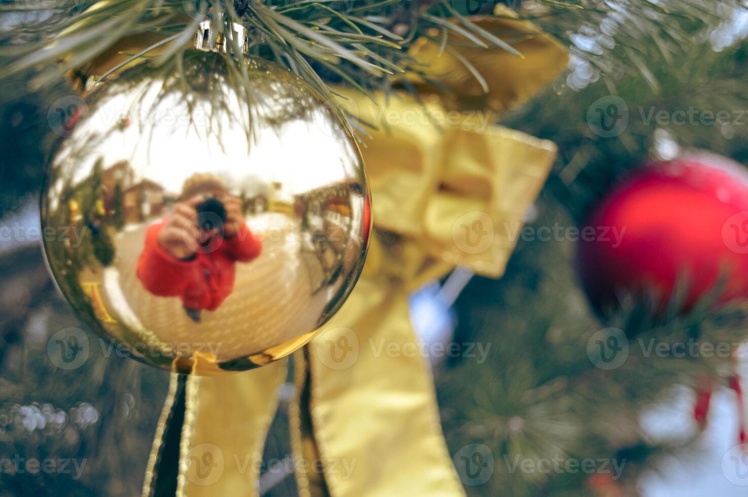 a golden toy on the Christmas tree in which a photographer with a camera is reflected. High quality photo