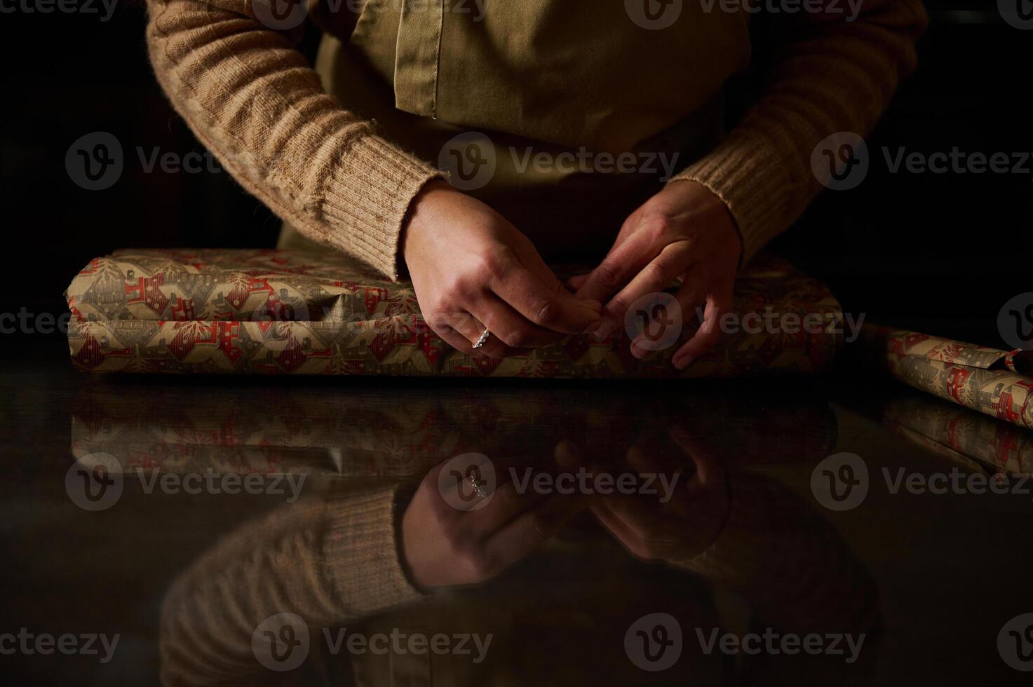 Hands wrapping a gift with patterned paper on reflective surface photo