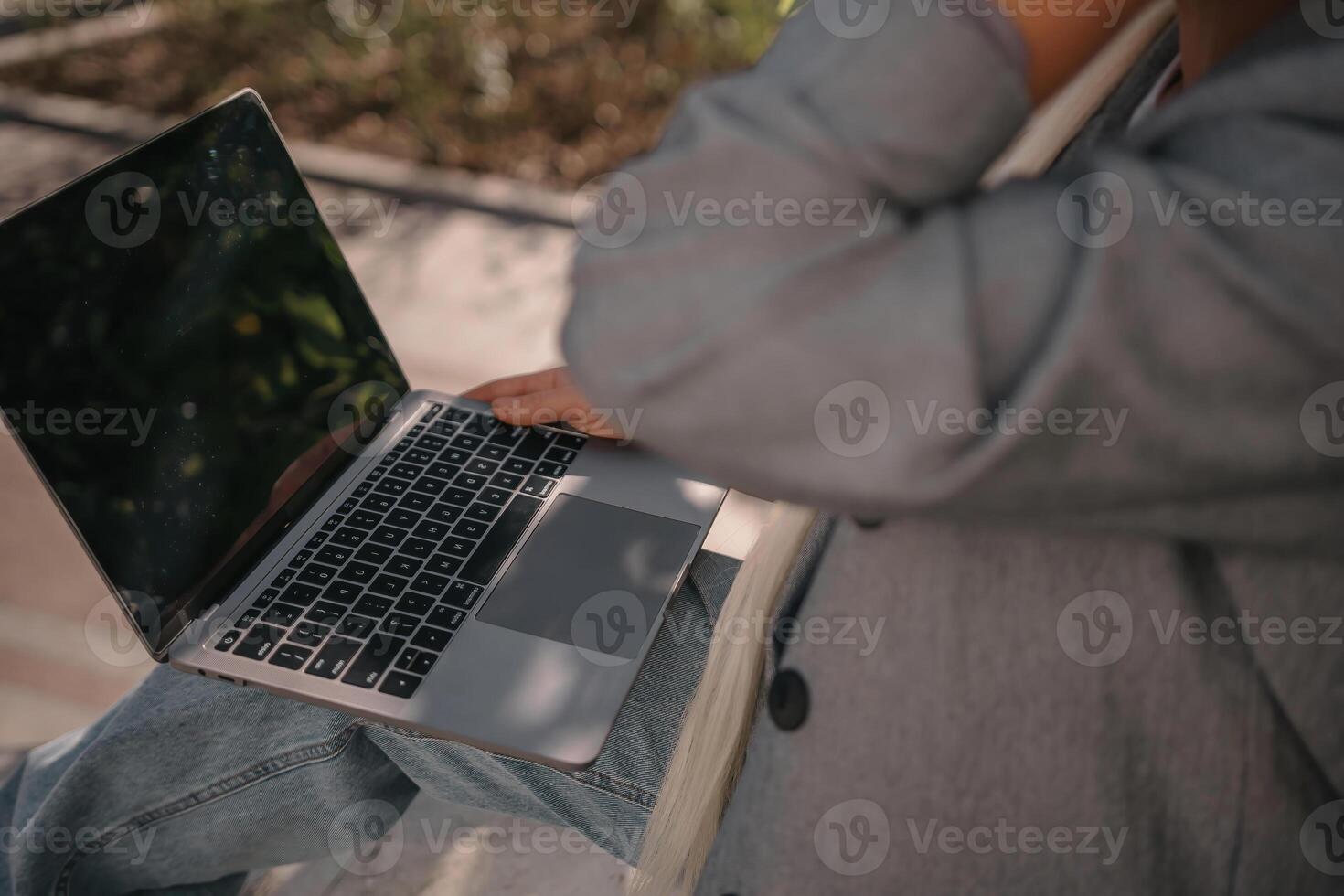 A person is sitting on a bench with a laptop open in front of them. They are typing on the keyboard, possibly working or browsing the internet. Concept of productivity and focus. photo