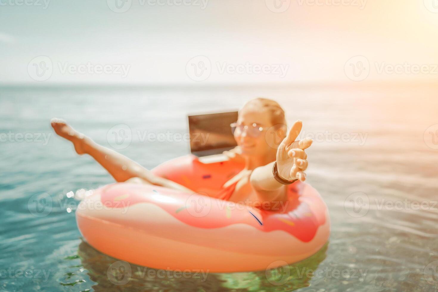 Woman laptop sea. Freelancer woman in sunglases floating on an inflatable big pink donut with a laptop in the sea. People summer vacation rest lifestyle concept photo