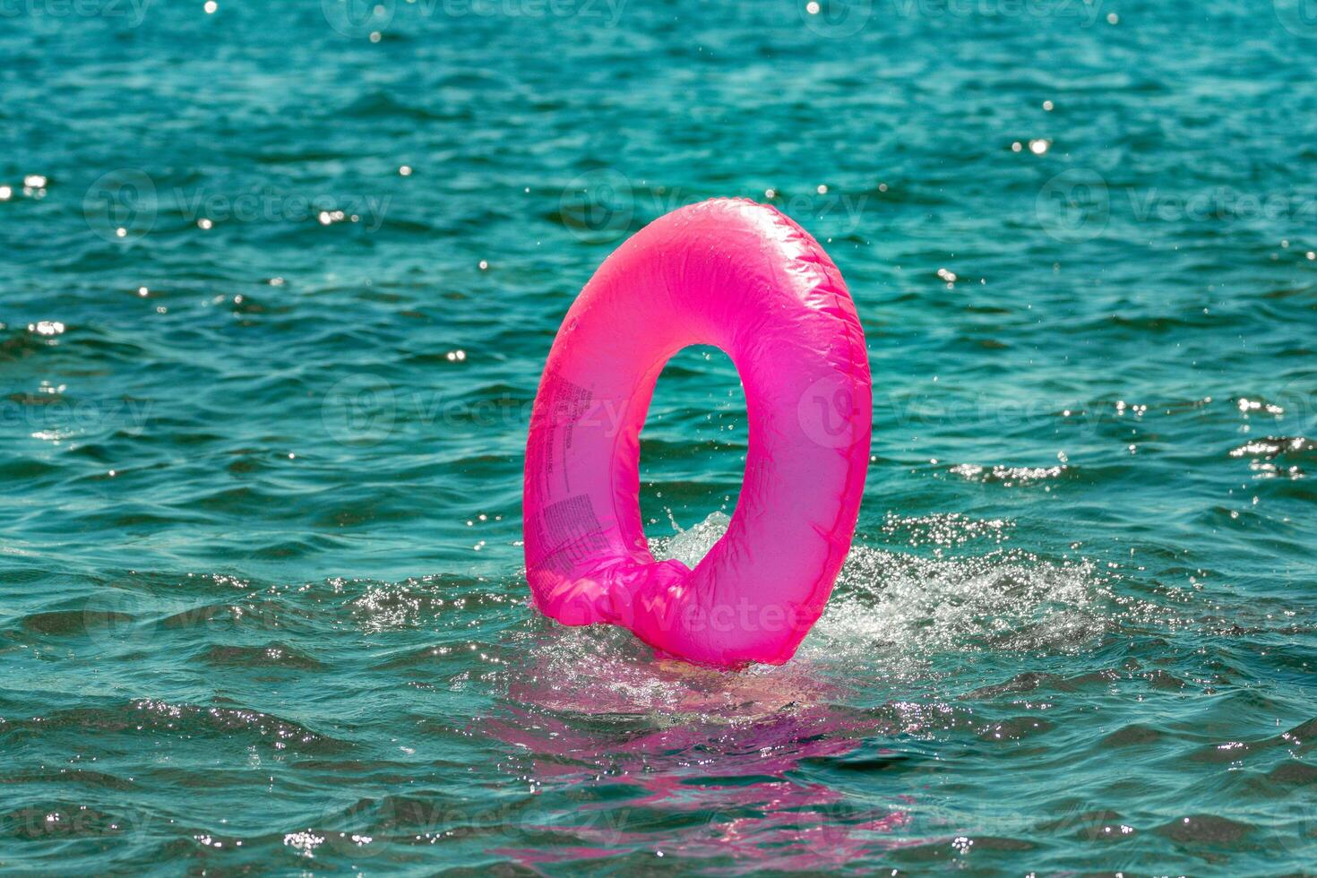 Inflatable Ring Water Ocean Summer. A pink inflatable ring floats in the turquoise water on a sunny summer day. photo