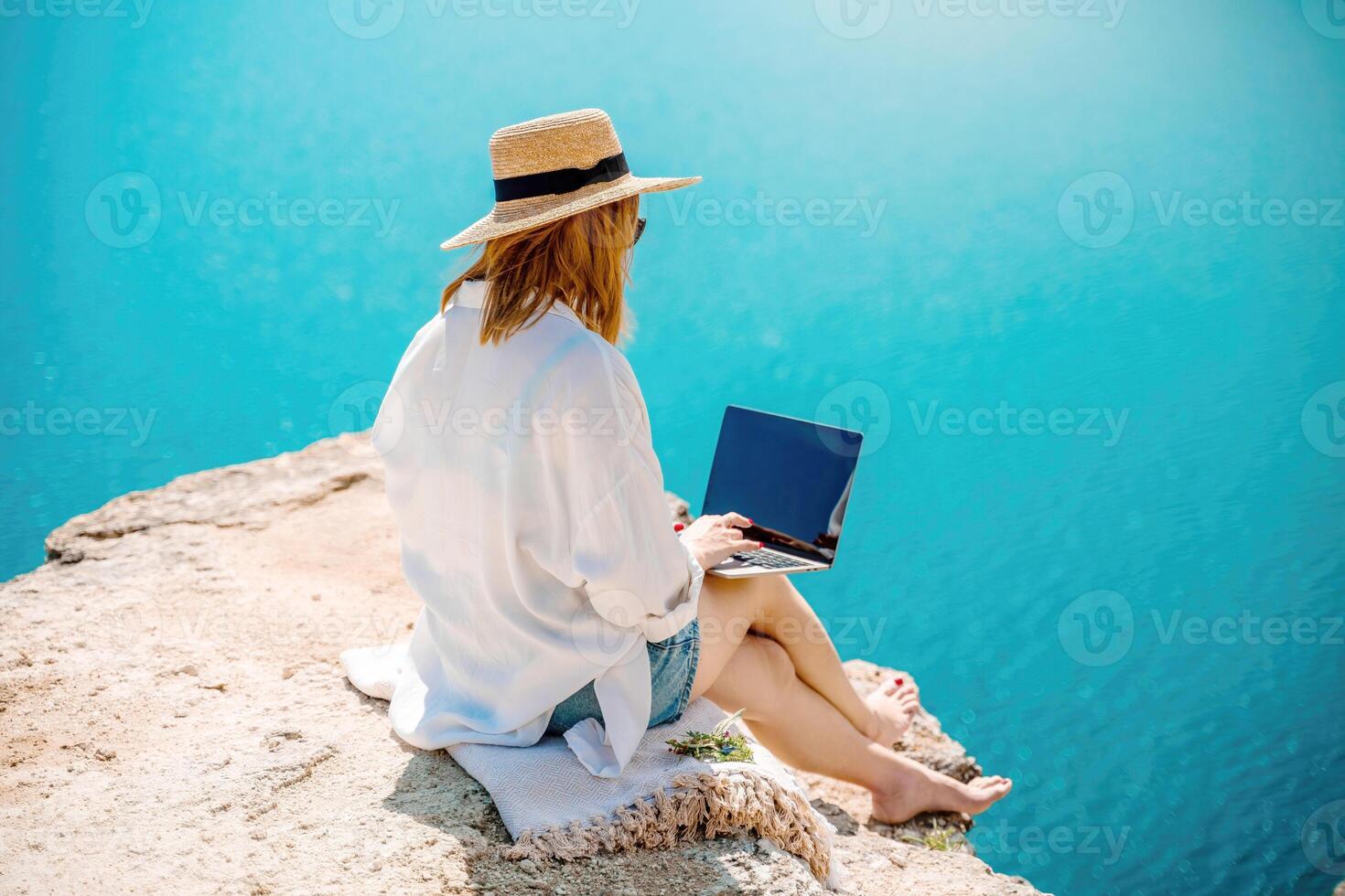 Freelance woman working on a laptop by the sea, typing away on the keyboard while enjoying the beautiful view, highlighting the idea of remote work. photo